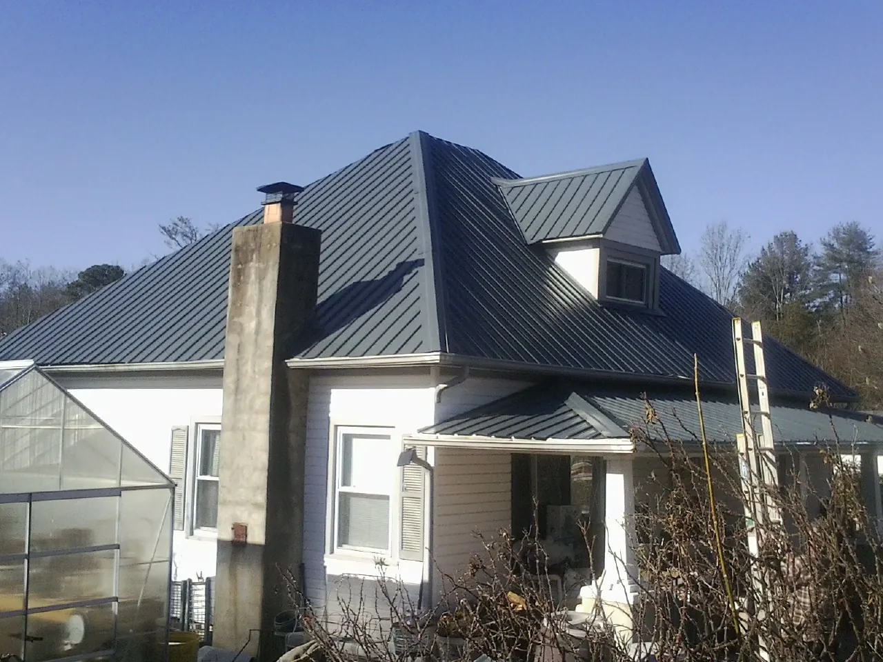 Dark blue standing seam metal roof on a white farmhouse with dormer — Slate & Tile Roof Repair by Roofing Brothers in Newmarket