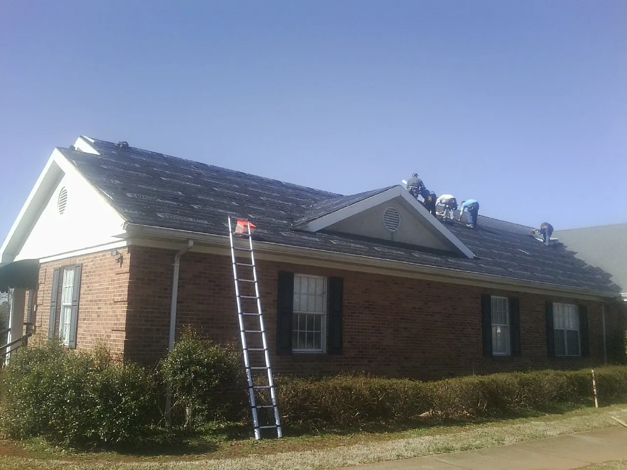 Crew tearing shingles off a brick ranch roof with a ladder set — Emergency Roof Repair work by our crew in Newmarket