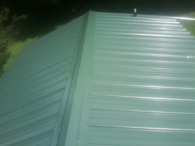 New green metal panels meeting at the ridge of a roof — Flat Roof Repair work by our crew in Newmarket