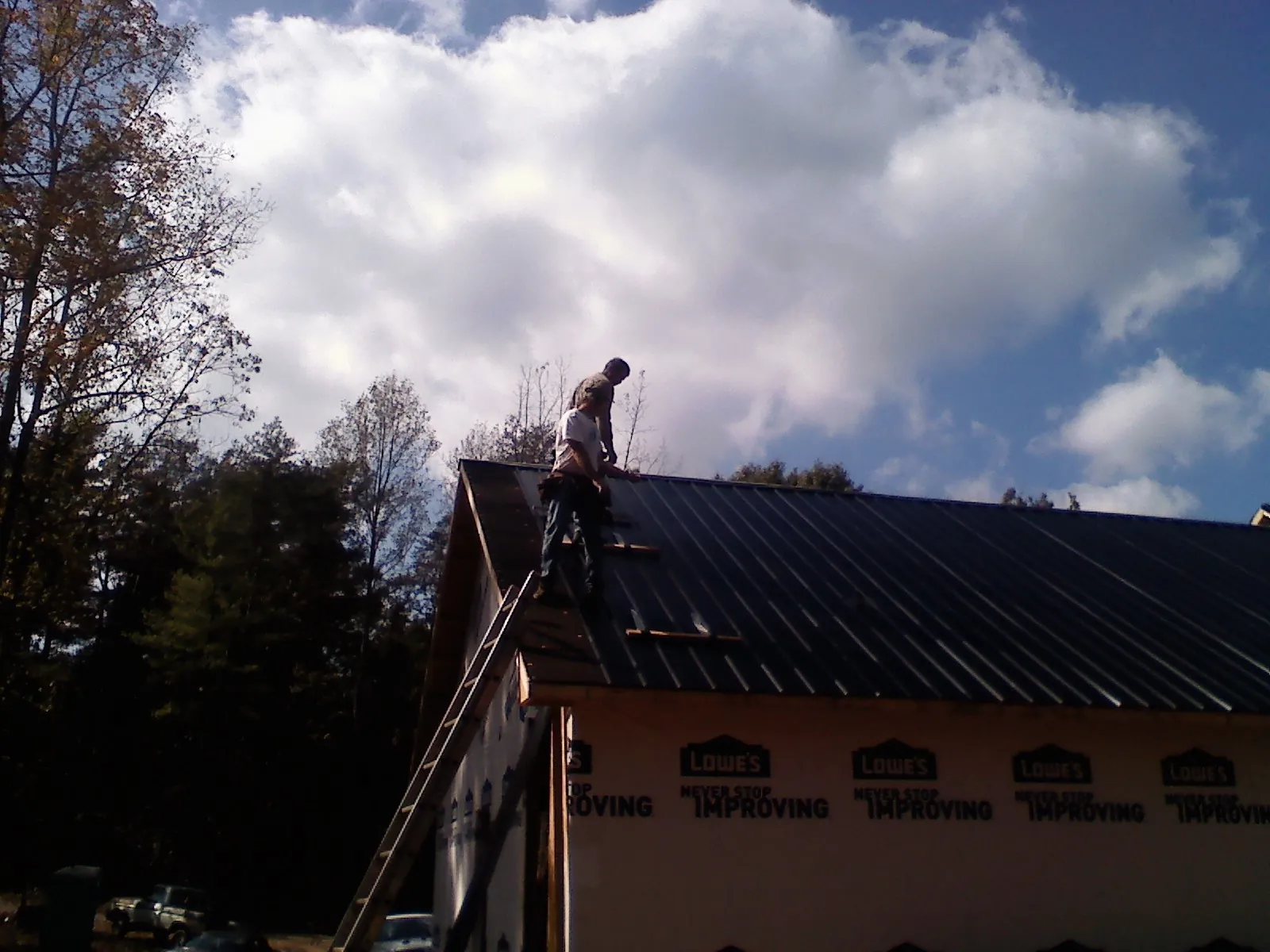 Roofer fastening dark metal panels high against a cloudy sky, from a Roof Inspection job in Newmarket