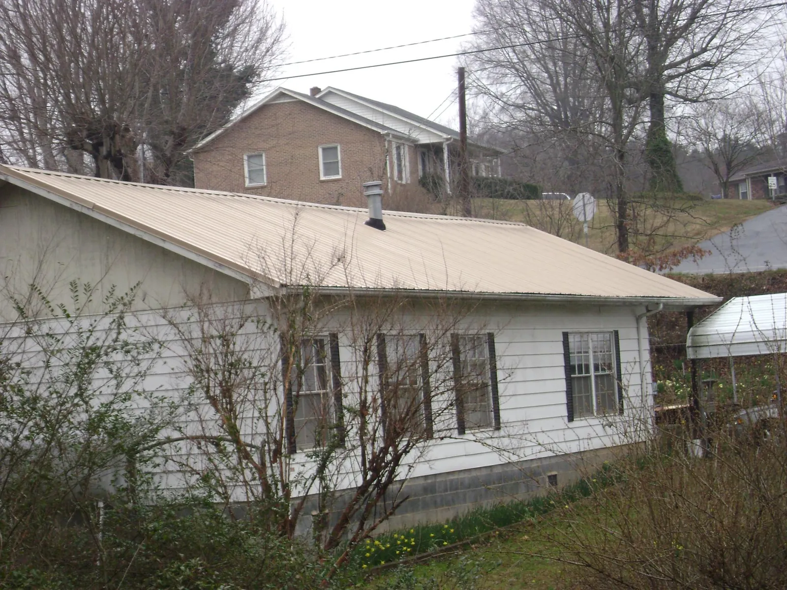 Tan metal roof on a white sided house set into a hillside — Commercial Roofing by Roofing Brothers in Newmarket